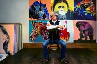 Andy Warhol sitting in front of paintings in his studio