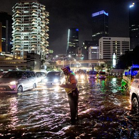 A man walks in shallow water flooding Jakarta