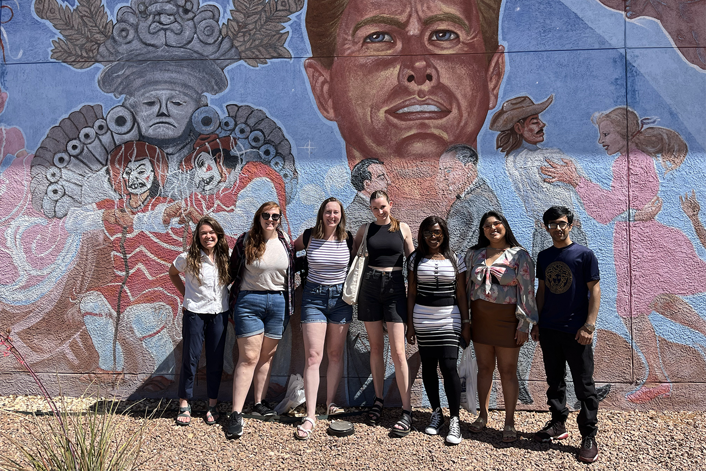 students posing in front of wall with mural