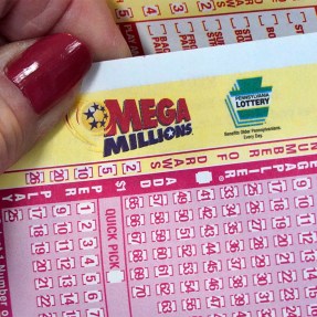 A hand holding a Mega Millions ticket with several other Mega Millions tickets in the background.