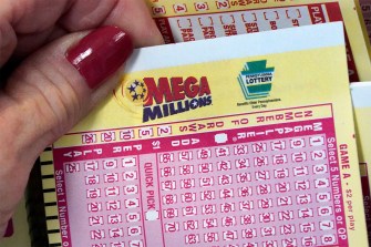A hand holding a Mega Millions ticket with several other Mega Millions tickets in the background.