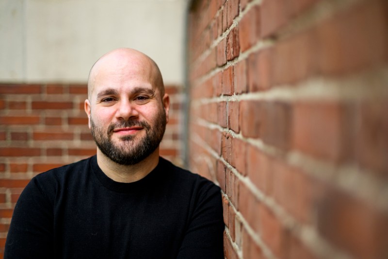 Portrait of Steve Granelli wearing a black long sleeve shirt and leaning up against a brick wall.