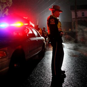 CT state trooper standing outside a police car at night in Newtown, CT