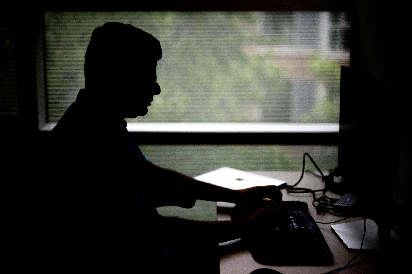 A silhouette of a person sitting in front of a computer.