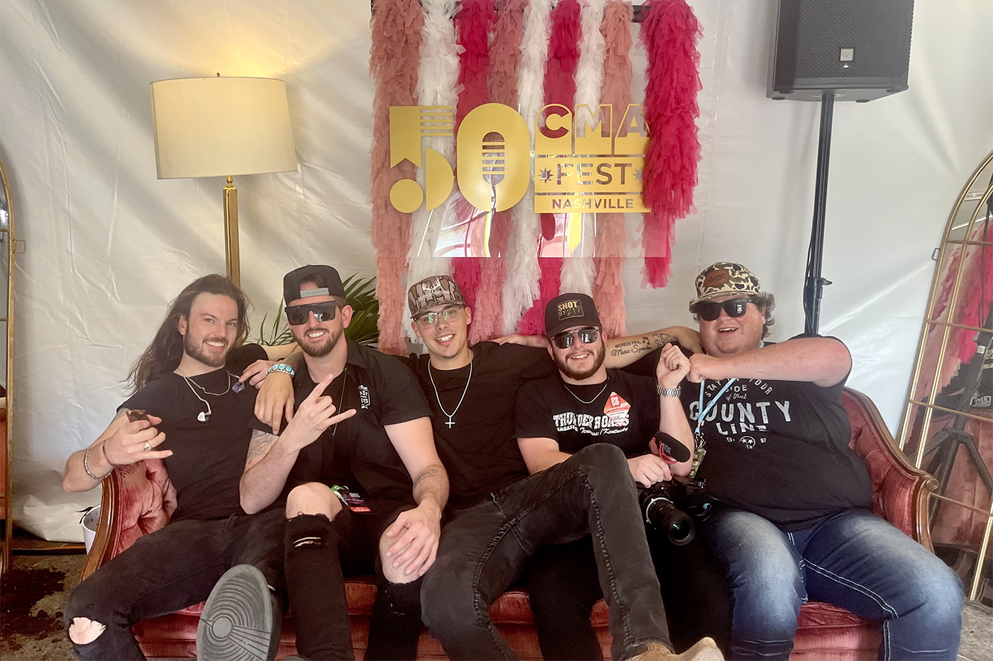 group of people wearing black t-shirts and sunglasses posing on a couch at the 50th CMA Fest in Nashville