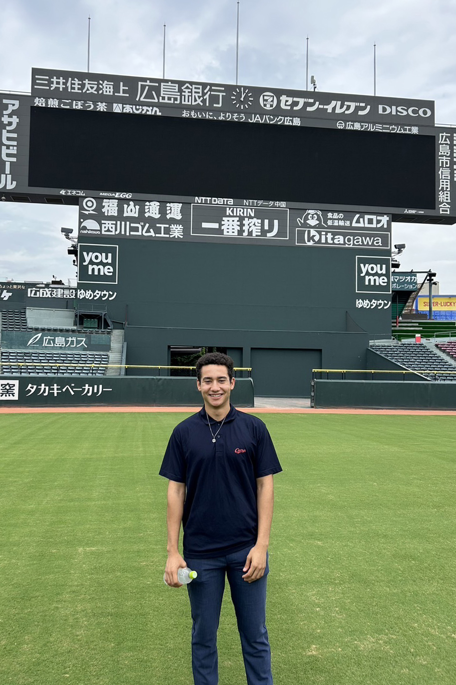Reece Calvin on a Japanese baseball field. The board behind says "Hiroshima".