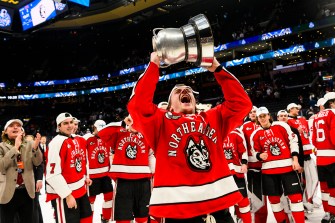 Northeastern mens ice hockey player lifting the Beanpot above his head after the team won the 2023 Men's Beanpot final.
