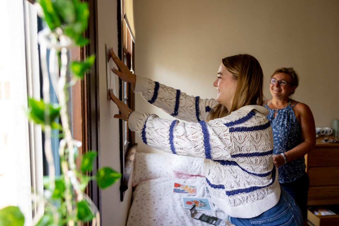 Nina Brunner placing decorations on her dorm wall while her mother stands behind her smiling.