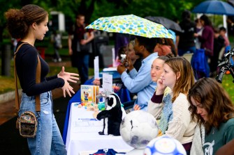 Students at the fall volunteer fair, some under umbrellas and some not.