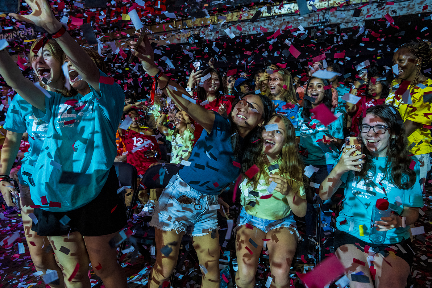 A crowd of students in Class 125 T-shirts cheer and take photos while confetti falls around them.