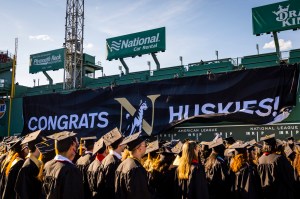 Graduates at Fenway Park in front of a banner that reads 'Congrats Huskies!'