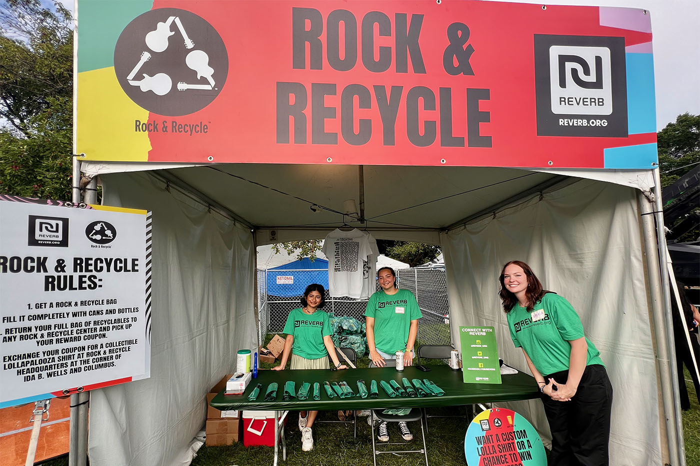 Three people posing under a white tent with a sign that reads "Rock & Recycle" on it.