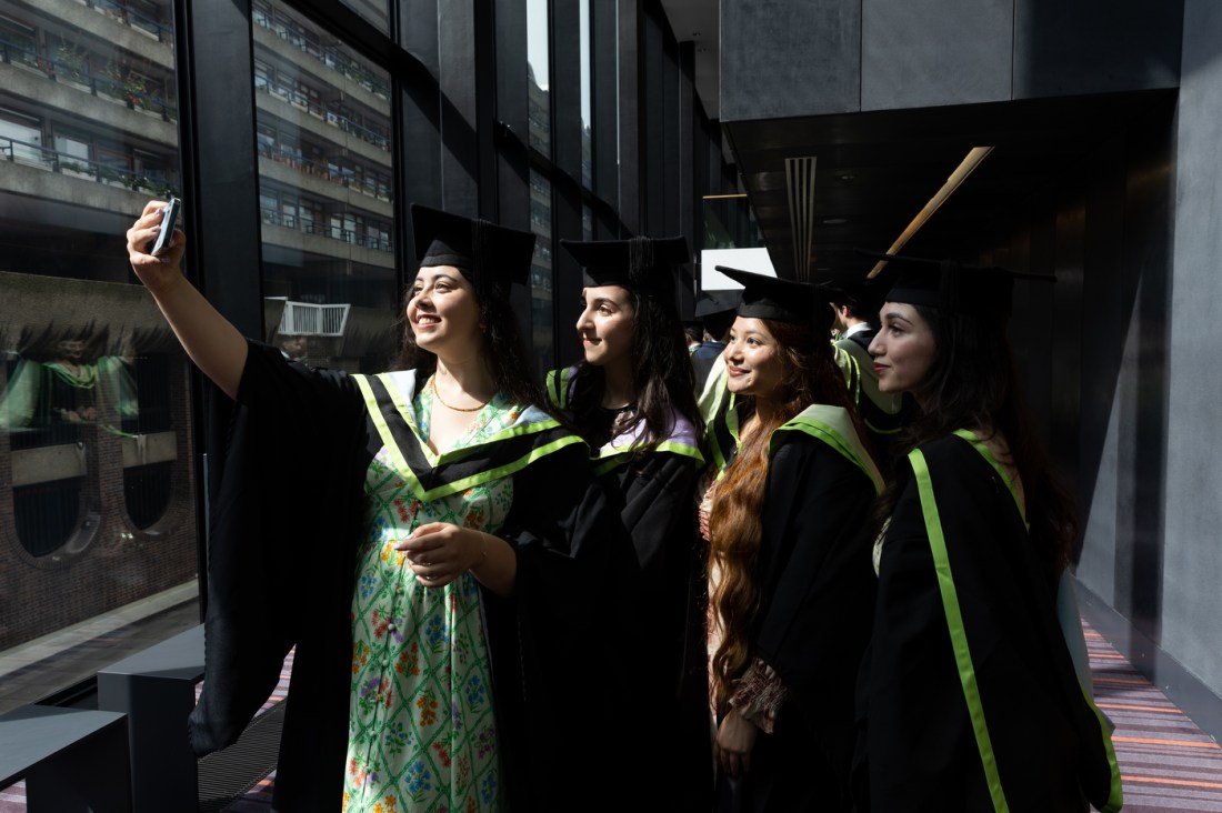 4 graduates posing for a selfie in their caps and gowns. 