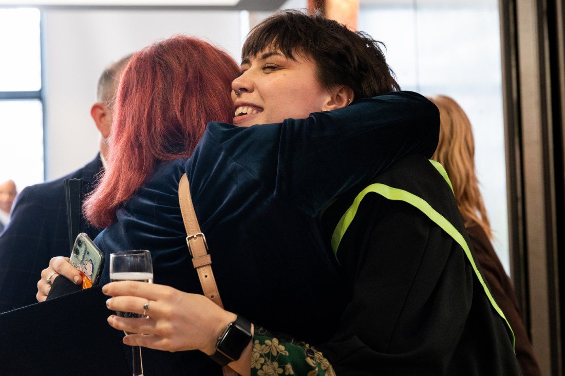 A graduate in their gown hugging a person with red hair. 