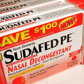 An orange and white box of Sudafed PE nasal decongestant.