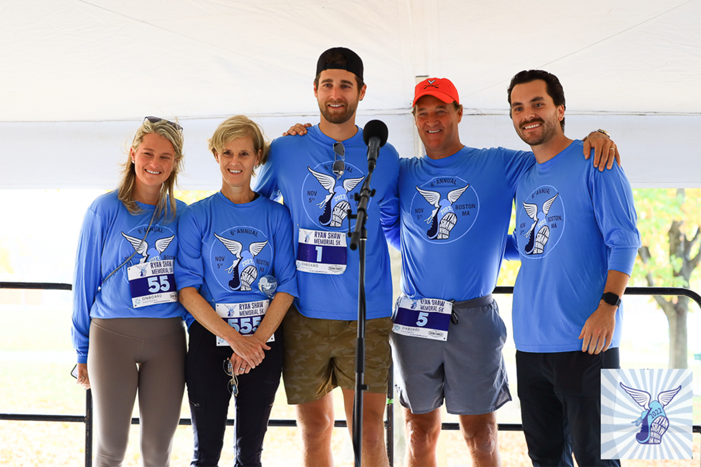 Group of people wearing blue Ryan Shaw Memorial 5K shirts posing together under a white tent. 