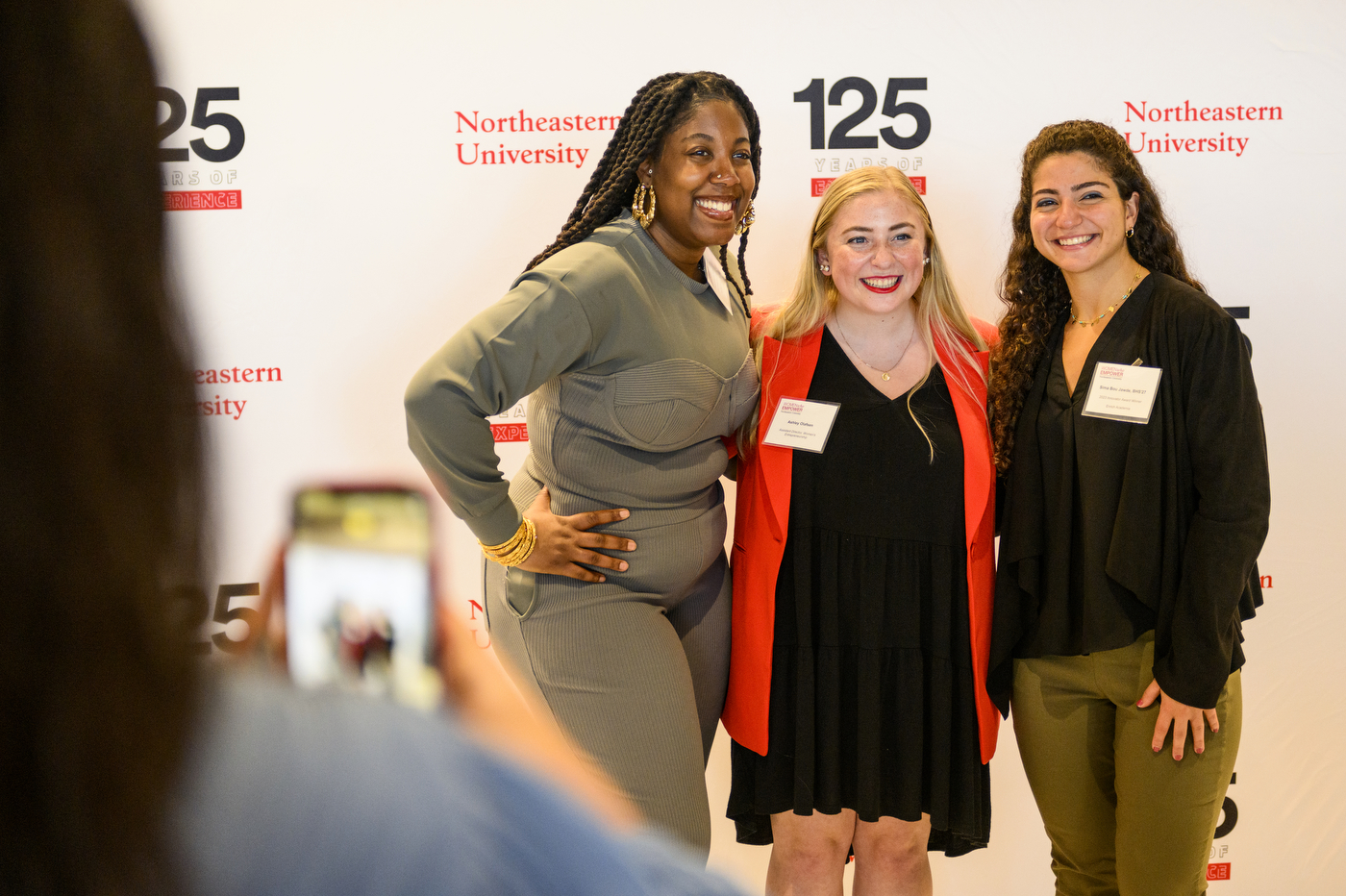 Participants pose for photos in front of a backdrop that says 125 Years of Experience, Northeastern University