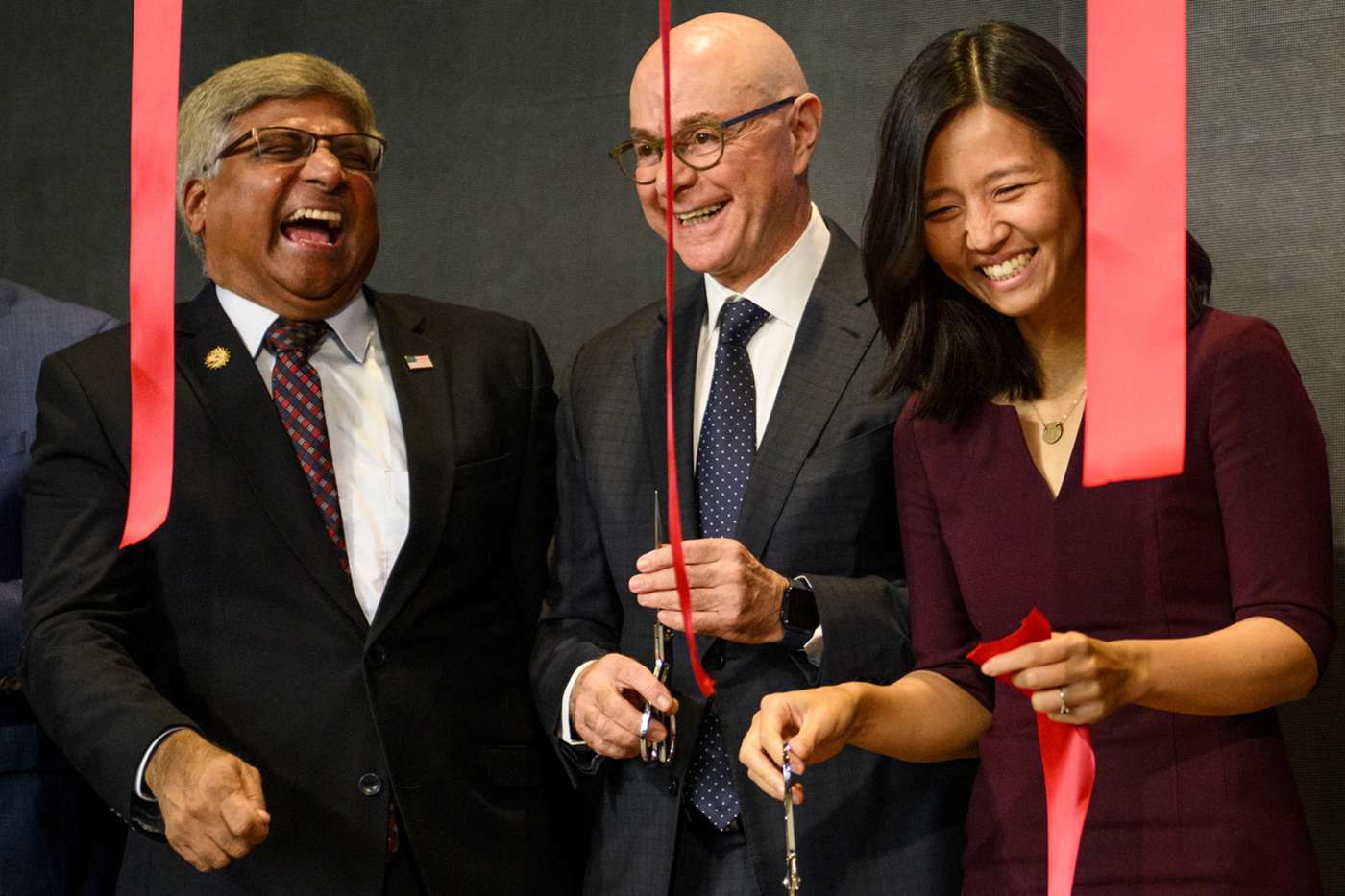 Sethuraman Panchanathan, Michelle Wu, and President Joseph Aoun laugh together while cutting red ribbons.