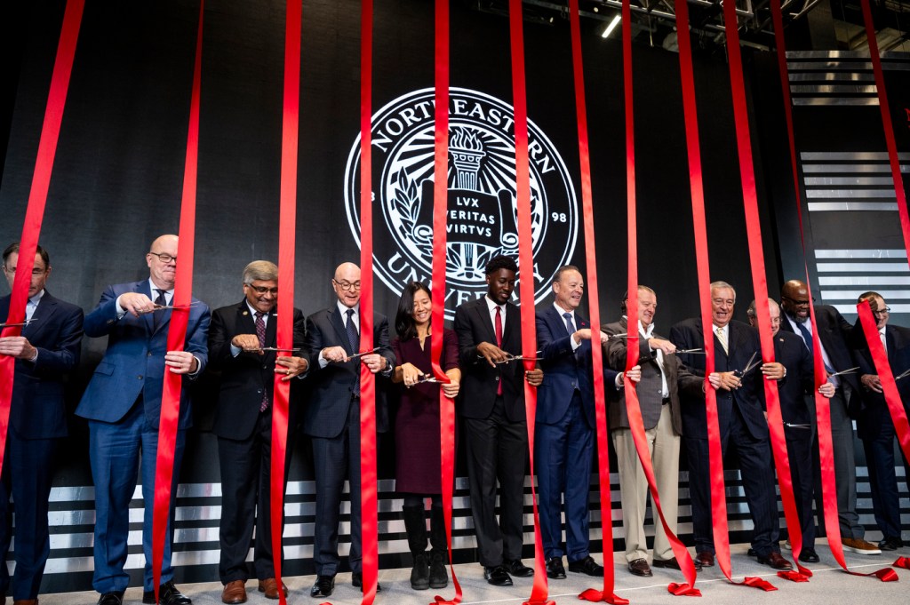 Over a dozen people stand on a stage for the EXP grand opening, cutting red ribbons.