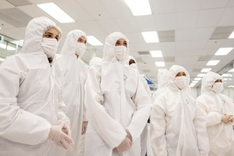 Students wearing white lab coats with hoods and white masks at Onto Innovations.