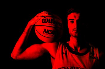 Northeastern basketball player stares at camera grasping ball upon his right shoulder