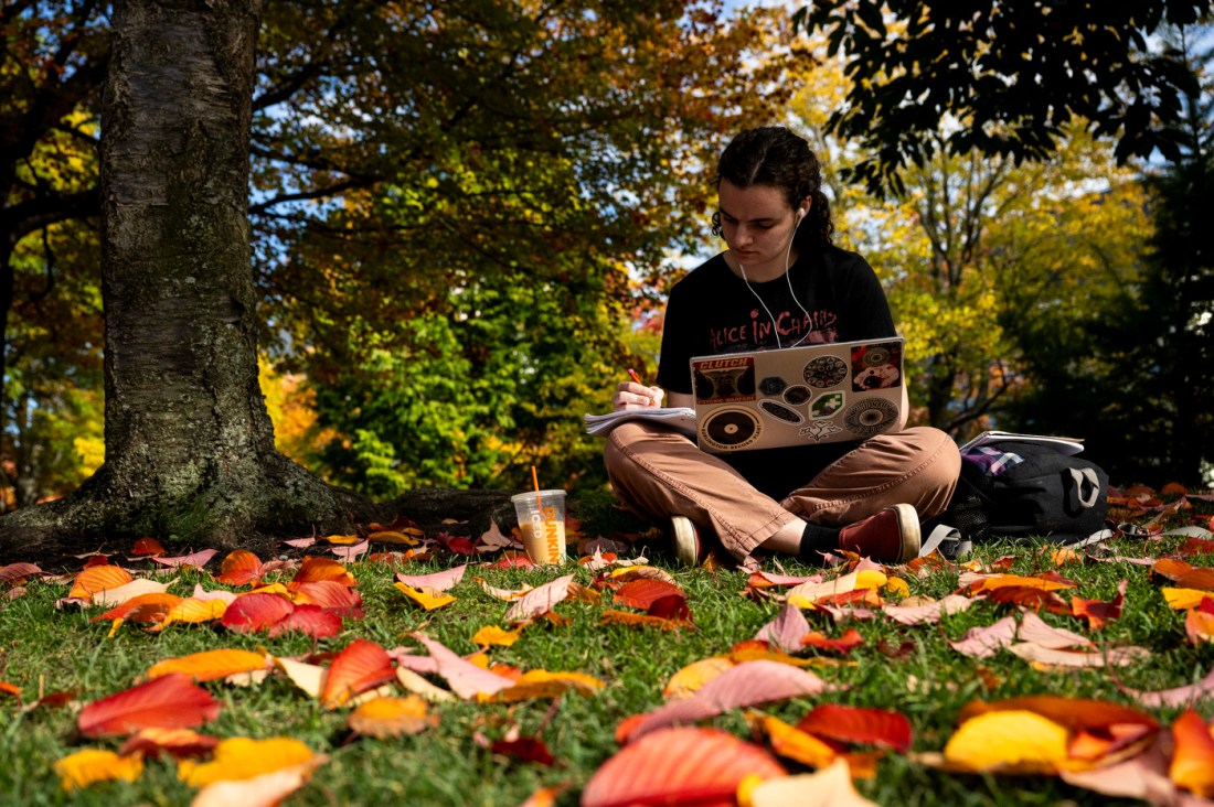 Maggie Heaney sitting on the common with her laptop and a notebook open in her lap. 