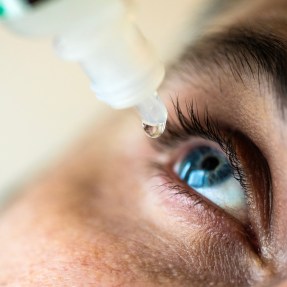 Person with blue eyes using eyedrops.