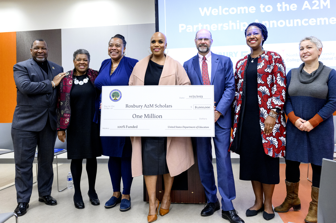 U.S. Rep. Ayanna Pressley posing for a photo with a group of people while holding a large check to Roxbury A2M Scholars for $1 million 