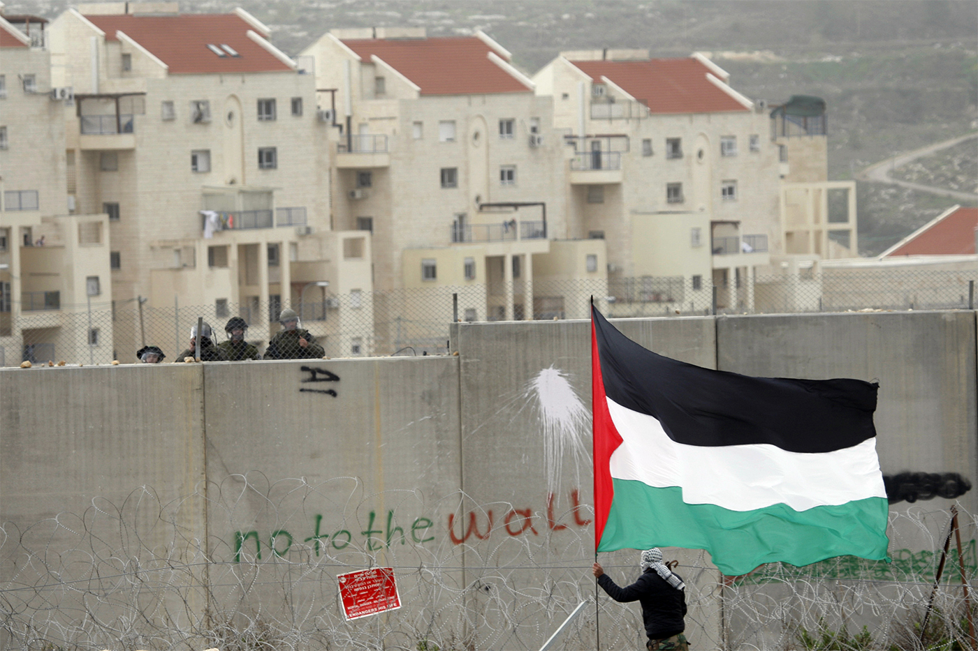 A protestor waving a Palestinian flag in front of Israeli troops on the other side of a wall in Modiin Illit. 