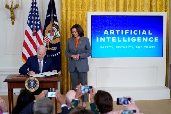 Kamala Harris standing over President Biden as he signs a new executive order on AI in the White House.