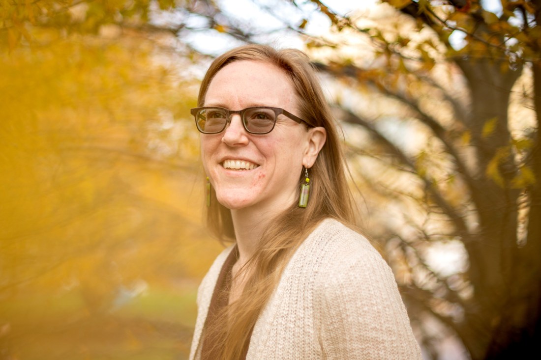 Deirdre Loughridge, associate professor of music at Northeastern University, smiling outdoors in front of autumn foliage.
