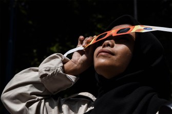 Student wearing solar eclipse glasses looking up at the sky.