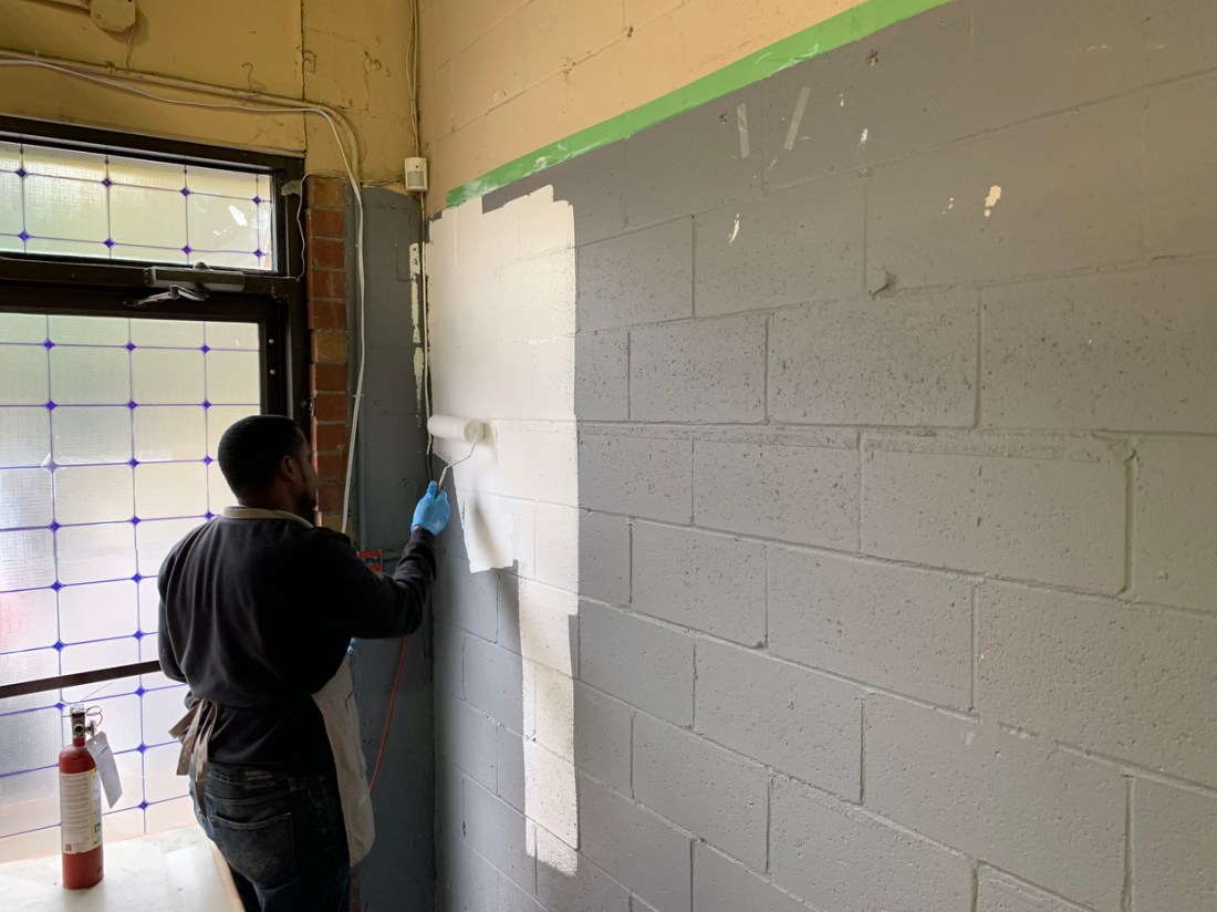 Student repainting a grey cement block wall white. 