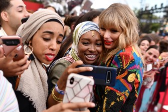 Multiple fans take pictures with Taylor Swift outside on a sunny day.
