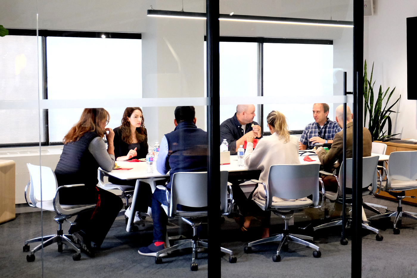 Group of people sitting around a conference table in a room with glass doors. 