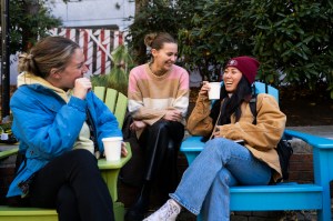 Three people sit outside while drinking apple cider.