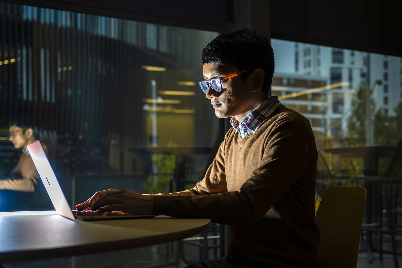 A person sits in front of a brightly lit laptop, studying.