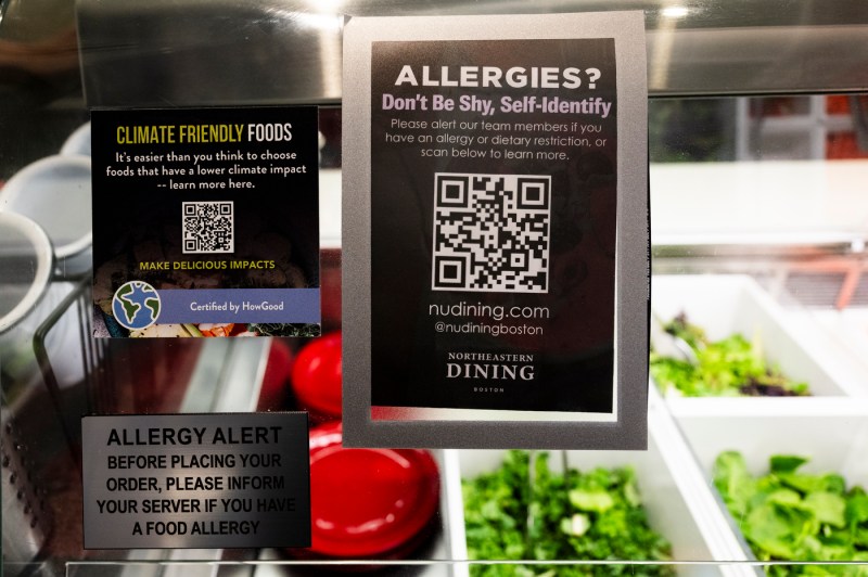 Posters on the glass protector of food in the United Table dining hall that say "Allergies? Don't be shy, self-identify," "climate friendly foods" and "Allergy alert". 