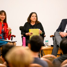 Mai’a Cross sitting with two panel speakers at the Crisis Conversation Series.