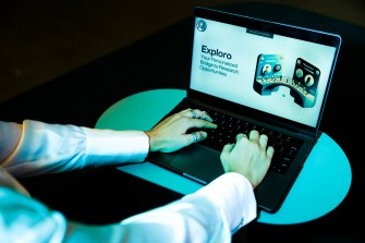 A person types on a laptop that displays black text: "Exploro."