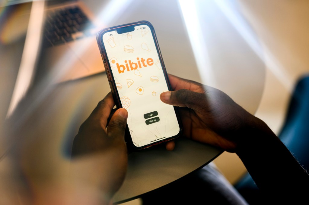 David Alade holding his phone displaying the startup image of the Bibite app.
