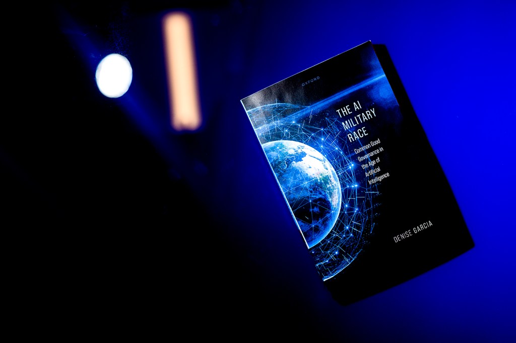 A blue and black-colored book titled "The AI Military Race" is suspended in the air in front of a blue background.