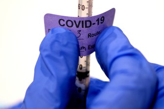 Gloved hand putting a COVID-19 label on a vaccine.
