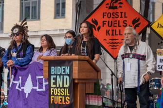 A woman from the Indigenous community speaking in front of a microphone at a rally against fossil fuels.
