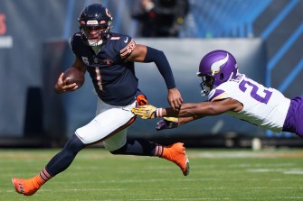 Chicago Bears quarterback running the ball while a Minnesota Vikings player dives to tackle him.