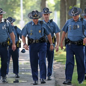 A group of six Massachusetts state police officers in uniform walking on a sidewalk.