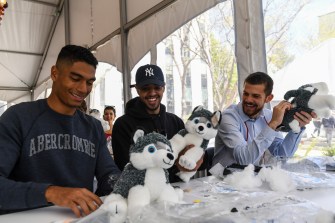 Students filling Husky toys with stuffing in a tent outside.