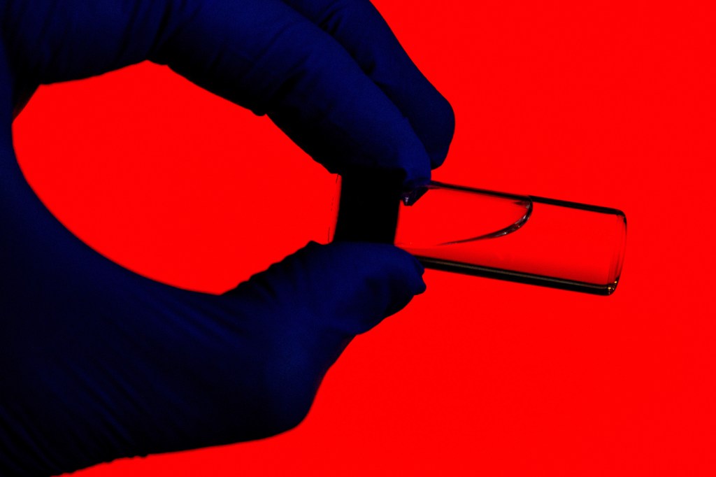 Silhouette of a person holding a vial test tube on a red background.
