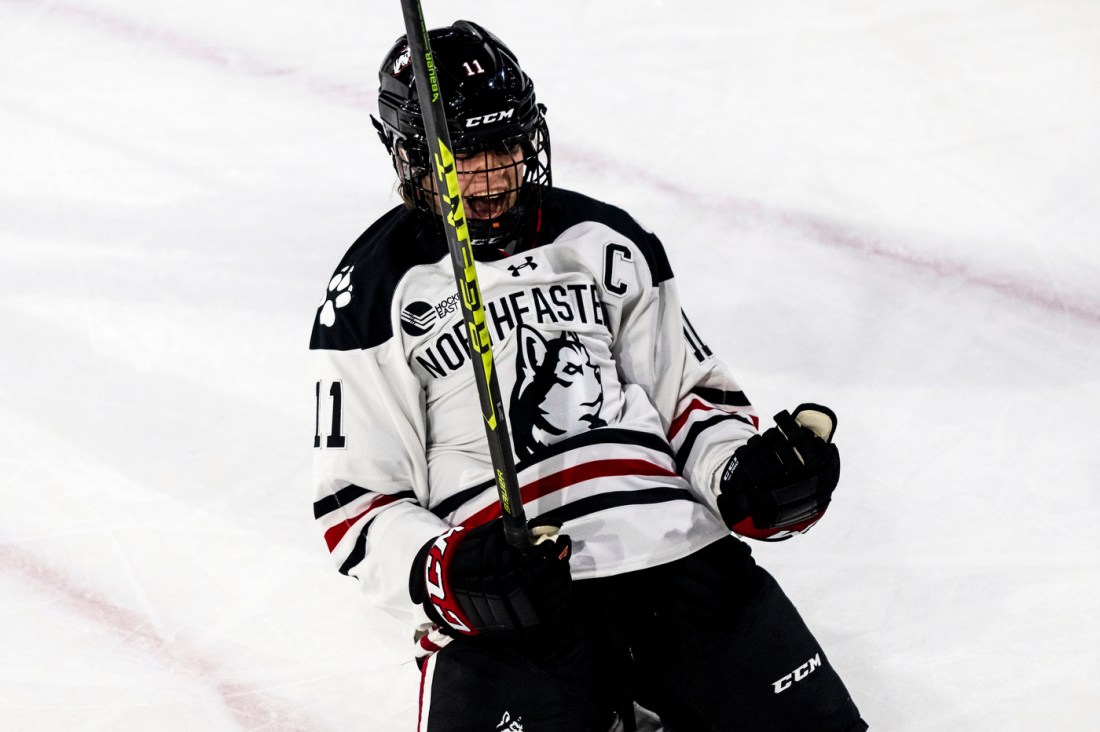 Northeastern womens hockey player cheering while sliding on the ice on their knees.