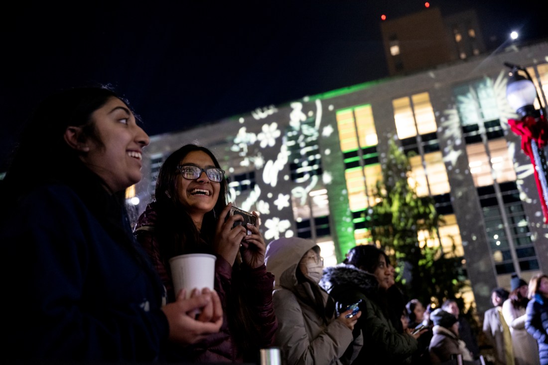 People smile outside while watching a holiday light show. 